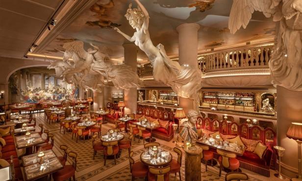 Das luxuriöse Interieur eines Restaurants mit Statuen, Wandmalereien und rotem Mobiliar.