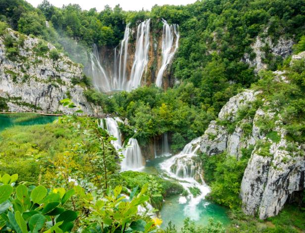 Mehrere Wasserfälle ergießen sich in den türkisfarbenen See, umgeben von üppigem Grün.