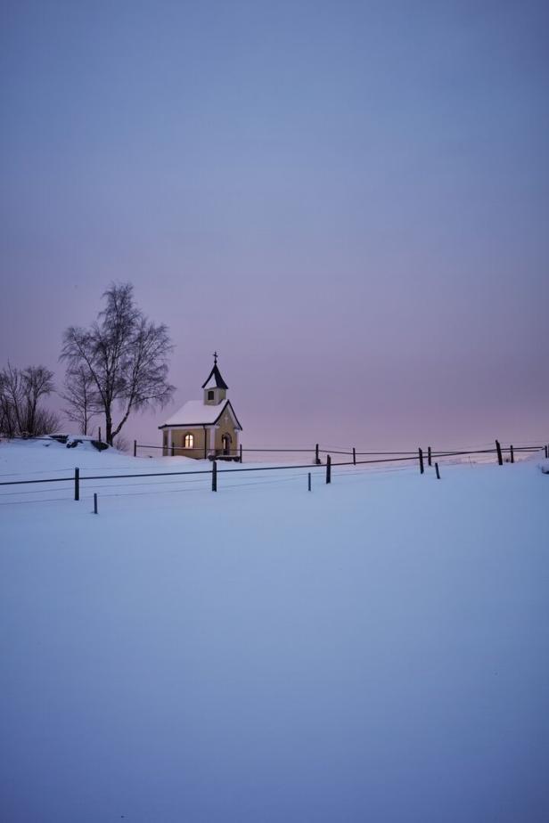 Eine kleine Kapelle steht im Winter auf einem schneebedeckten Feld.