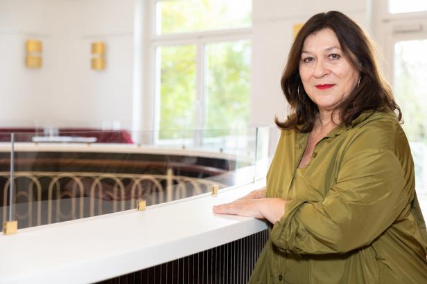 Eine Frau in einer olivgrünen Bluse steht an einem Geländer.