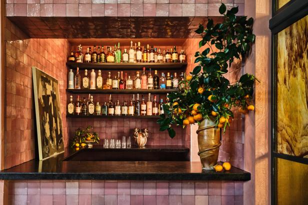 Eine Bar mit rosa Fliesen, gefüllt mit Spirituosenflaschen und einem Arrangement aus Mandarinenbaumzweigen.