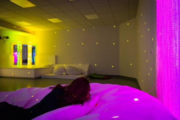 Eine Frau liegt auf einem Wasserbett in einem Raum mit verschiedenen Lichteffekten.