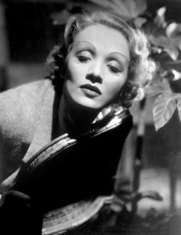 Marlene Dietrich posiert mit geschlossenen Augen und einer Handtasche.