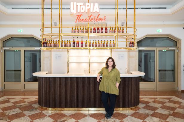 Eine Frau steht an der „Utopia Theaterbar“, hinter der sich Regale mit Getränkeflaschen befinden.
