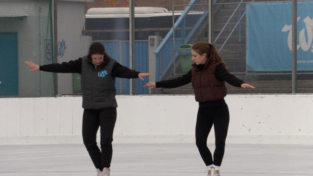 Zwei Frauen stehen auf einer Eisbahn und üben Eiskunstlauf.