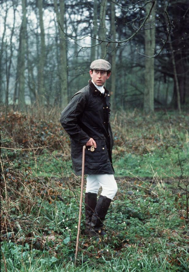 Prinz Charles in Jagdkleidung mit Stock in einem Wald.
