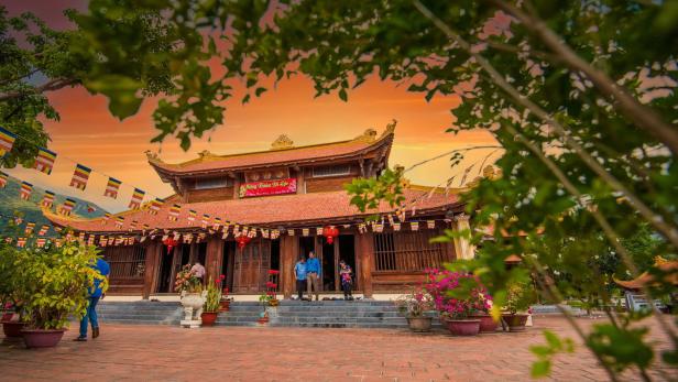Ein buddhistischer Tempel mit roten Ziegeln und bunten Fahnen bei Sonnenuntergang.
