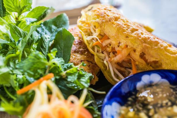 Ein vietnamesischer Crêpe, Banh Xeo, gefüllt mit Gemüse und Kräutern, wird mit einem Dip serviert.
