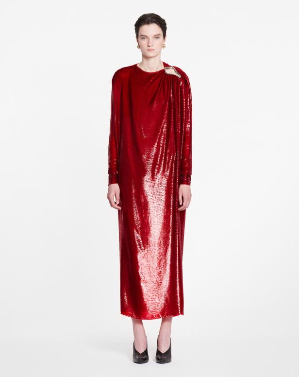 Eine Frau trägt ein langes, rotes Paillettenkleid mit einem ausgeschnittenen Detail an der Schulter.