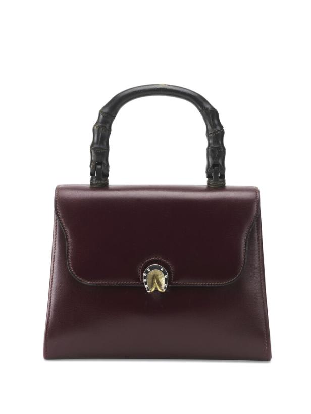 Eine bordeauxrote Handtasche mit einem Griff aus Bambus und einem goldenen Verschluss in Hufeisenform.