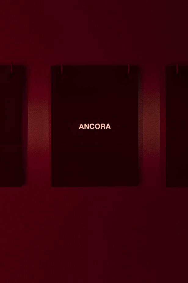 Ein Schild mit der Aufschrift „Ancora“ an einer roten Wand.