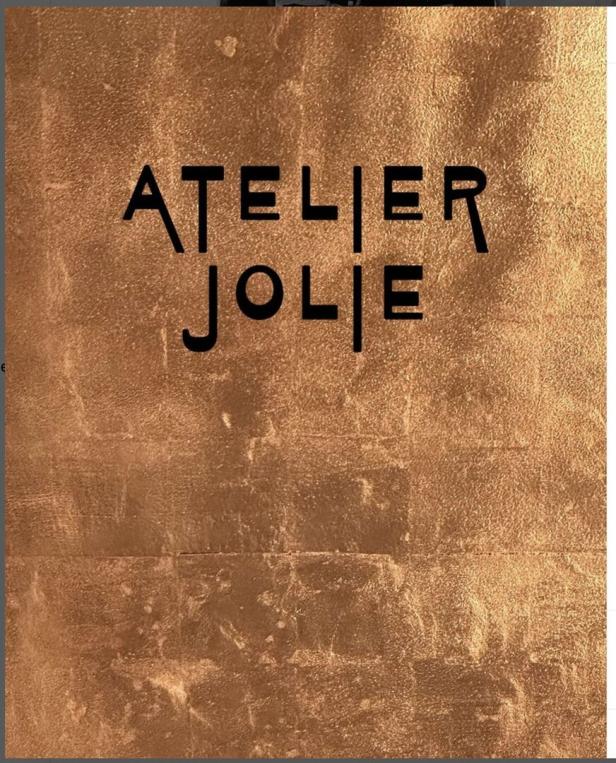 Das Logo von „Atelier Jolie“ auf einem goldenen Hintergrund.