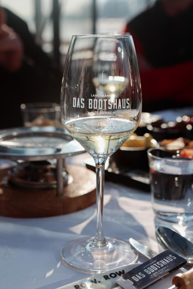 Ein Weinglas mit dem Schriftzug „Das Bootshaus“ steht auf einem Tisch.
