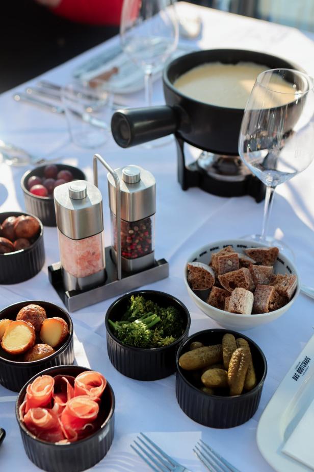 Ein Tisch mit Käsefondue, Brot, Gemüse, Kartoffeln und Wurst zum Dippen.