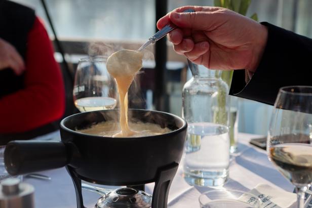 Eine Person hebt mit einem Löffel dampfendes Käsefondue aus einem Topf.