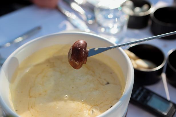 Ein Champignon wird in einen Topf mit Käsefondue getunkt.