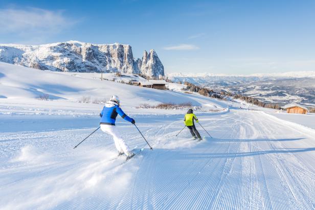 Zwei Skifahrer fahren auf einer präparierten Piste mit Blick auf die Dolomiten.