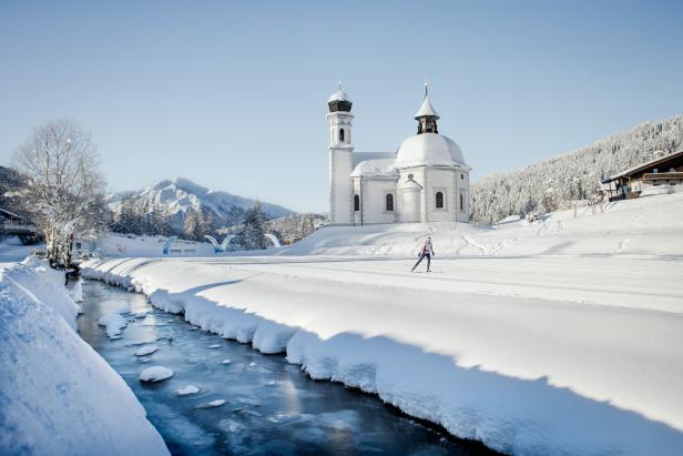 Eine Frau läuft Ski vor der verschneiten Seekirche in Seefeld, Tirol.