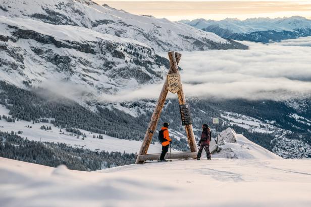 Zwei Personen stehen an einem Aussichtspunkt im Skigebiet Laax mit Blick auf verschneite Berge und Wolken.
