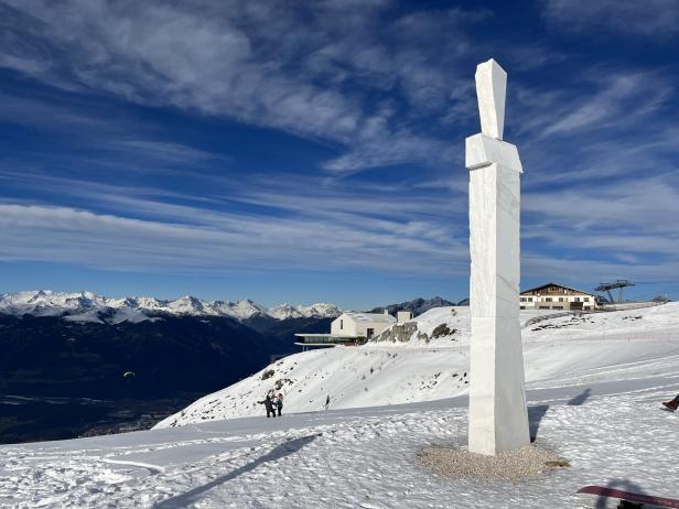 Eine weiße Skulptur steht auf einem schneebedeckten Berg mit Blick auf eine Bergkette.