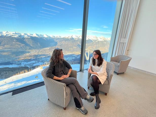 Zwei Frauen sitzen in Sesseln mit Blick auf eine verschneite Berglandschaft.
