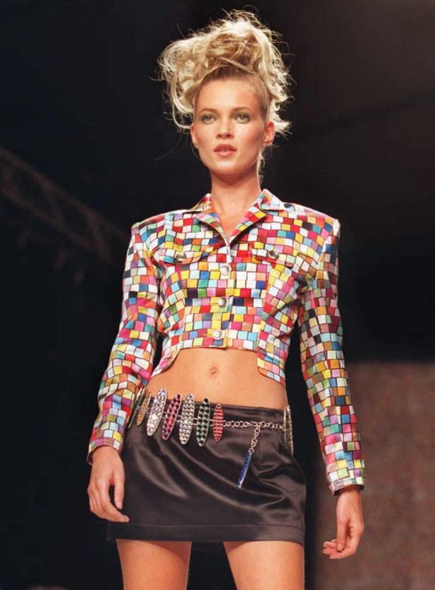 Kate Moss trägt ein buntes, kariertes Jackett und einen schwarzen Minirock auf dem Laufsteg.