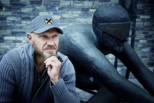 Ein Mann mit Kappe sitzt neben einer Skulptur.