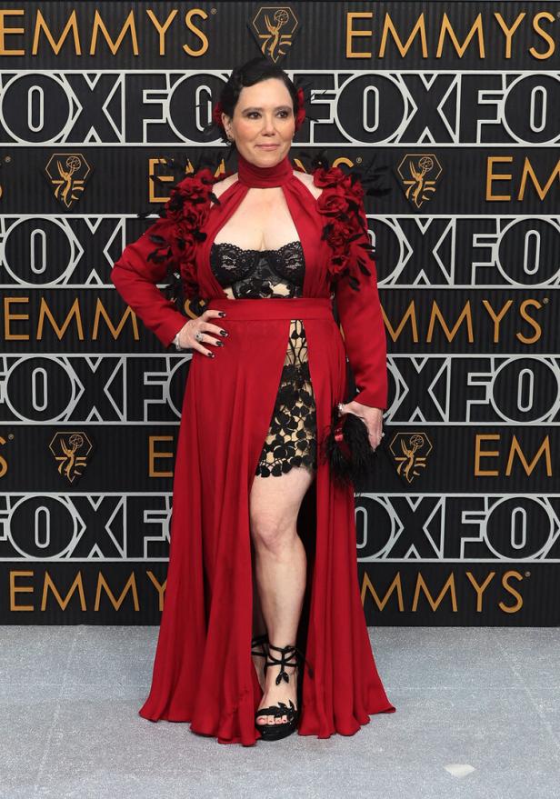 Eine Frau in einem roten Kleid mit Blumenapplikationen posiert vor einem „Emmys“-Hintergrund.