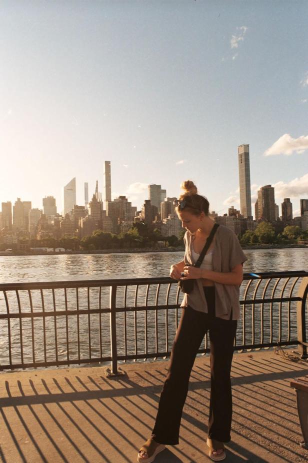 Eine Frau steht bei Sonnenschein vor der New Yorker Skyline und Blick zu Boden