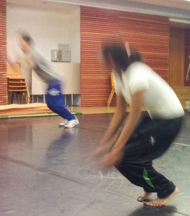 Zwei Personen üben barfuß in einem Raum mit Holzwandelementen.