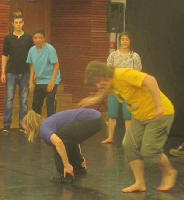 Eine Gruppe junger Leute tanzt oder probt in einem Raum mit Holzwänden.