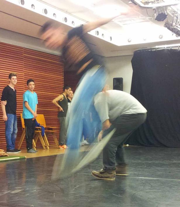 Ein junger Mann springt über einen anderen, während eine Gruppe Jugendlicher zusieht.