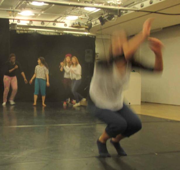 Eine Tänzerin springt vor einer Gruppe von Mädchen auf einer Bühne.