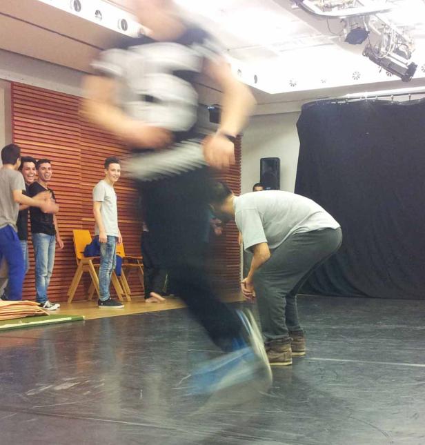 Eine Gruppe junger Männer in einem Raum, einer springt in Bewegung.