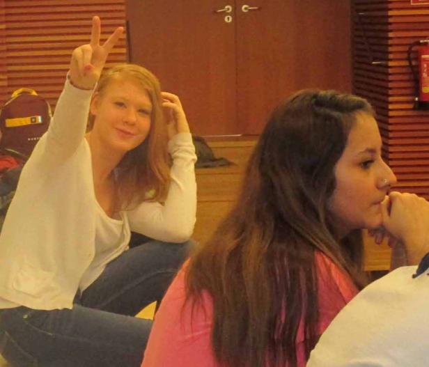 Zwei junge Frauen sitzen in einem Raum, eine zeigt ein Victory-Zeichen.