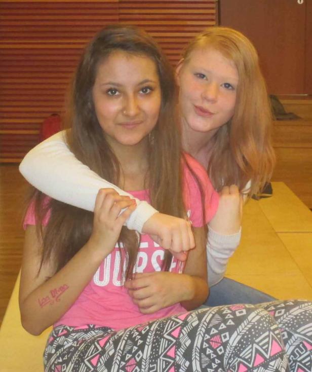 Zwei junge Frauen umarmen sich und lächeln in die Kamera.