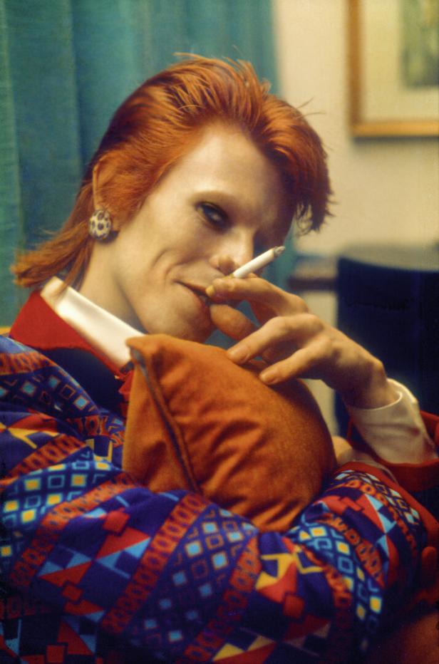 David Bowie mit roten Haaren, ein Zigarette rauchend, in einem bunten Blazer.