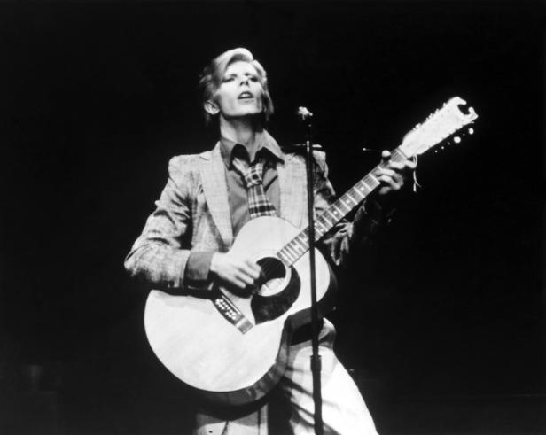 David Bowie spielt Gitarre und singt auf der Bühne.