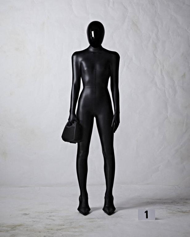 Eine schwarz gekleidete, vermummte Person hält eine Handtasche.