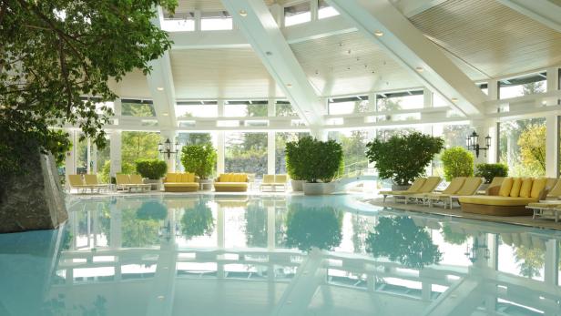 Ein Innenpoolbereich mit Liegestühlen und üppiger Vegetation unter einem Glasdach.