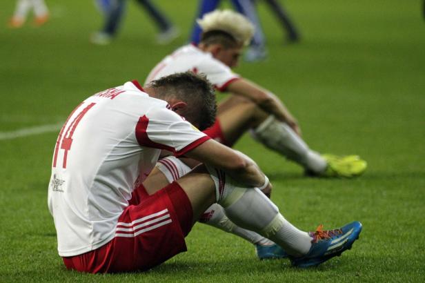 Zwei Fußballspieler sitzen enttäuscht auf dem Rasen.