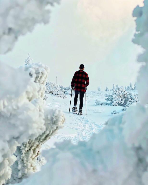 Ein Mann mit Schneeschuhen und Wanderstöcken wandert durch eine verschneite Landschaft.