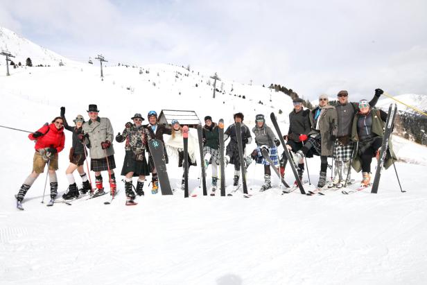 Eine Gruppe von Menschen in Kilts und Skikleidung steht auf einer Skipiste.