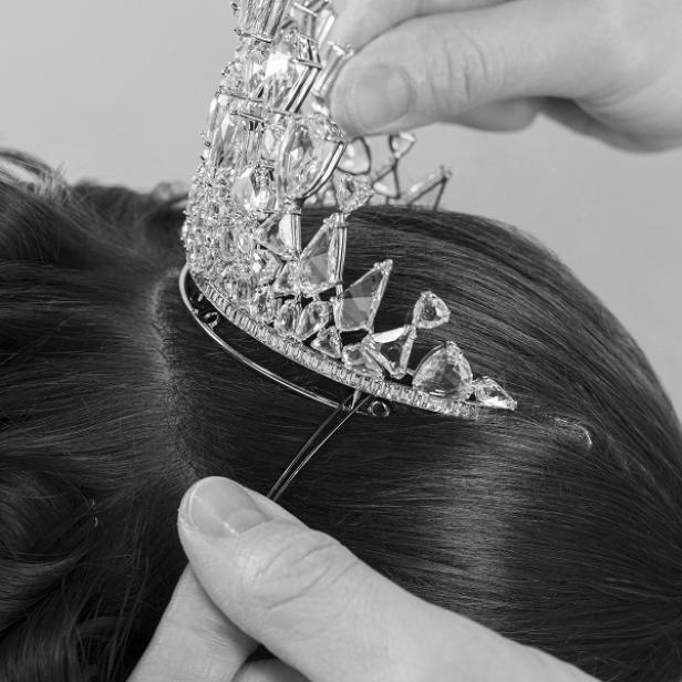 Eine funkelnde Tiara wird in eine dunkle Hochsteckfrisur eingesetzt.