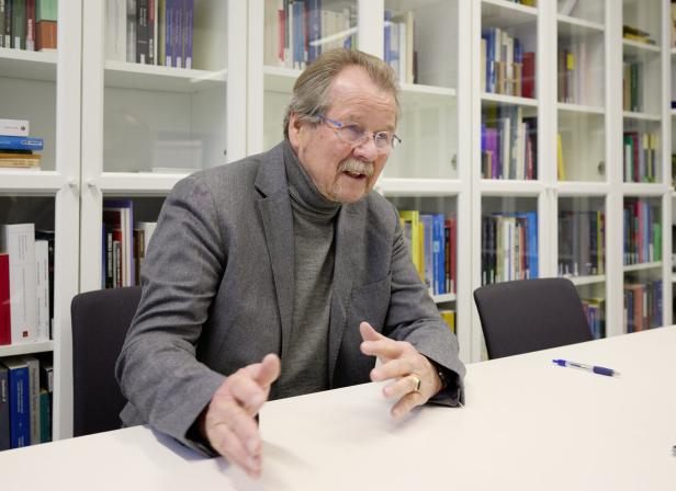 Manfred Nowak sitzt gestikulierend an einem Tisch vor einem Bücherregal