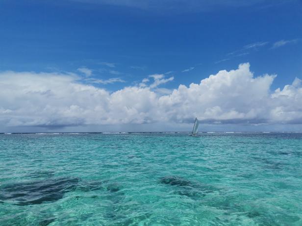 Ein Segelboot fährt auf dem türkisfarbenen Wasser unter einem blauen Himmel mit Wolken.