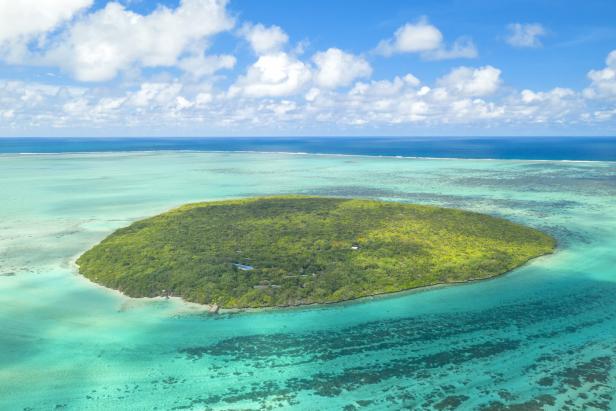 Eine grüne Insel liegt inmitten des türkisfarbenen Ozeans unter einem blauen Himmel mit Wolken.