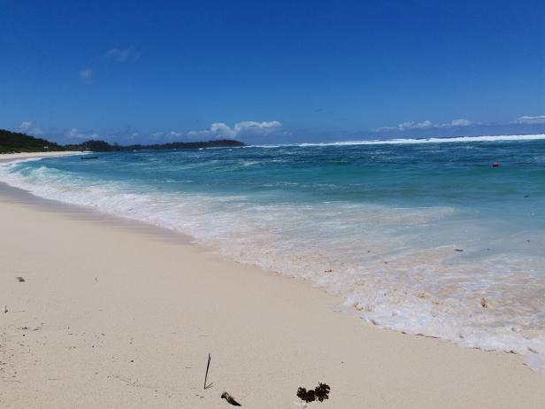 Ein ruhiger Strand mit weißem Sand und türkisfarbenem Wasser unter blauem Himmel.