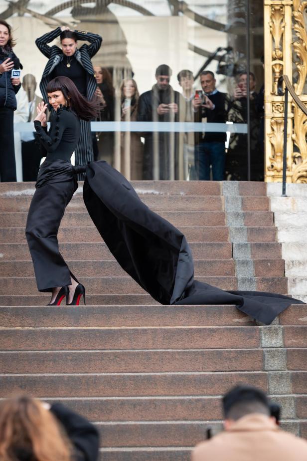 Eine Frau in einem schwarzen Hosenanzug mit Schleppe steigt eine Treppe hinunter.