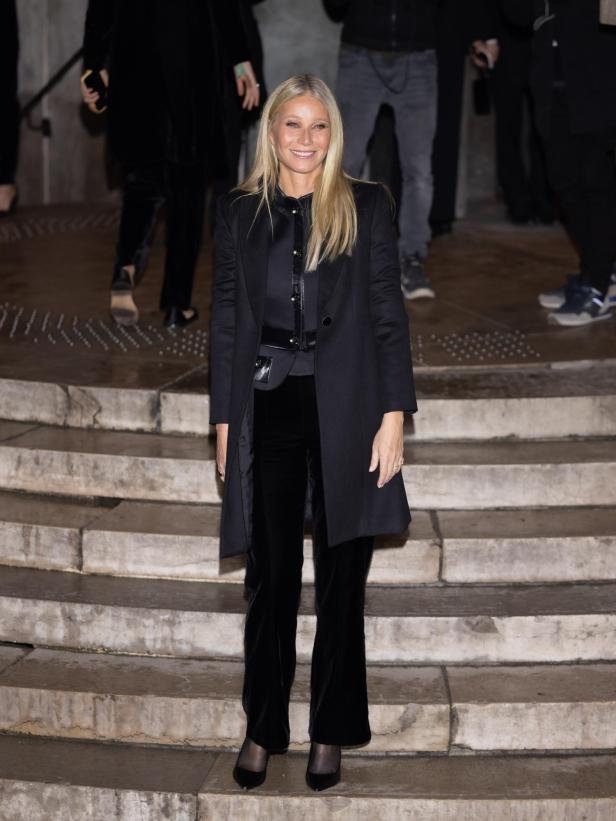 Gwyneth Paltrow posiert auf einer Treppe in einem schwarzen Hosenanzug.
